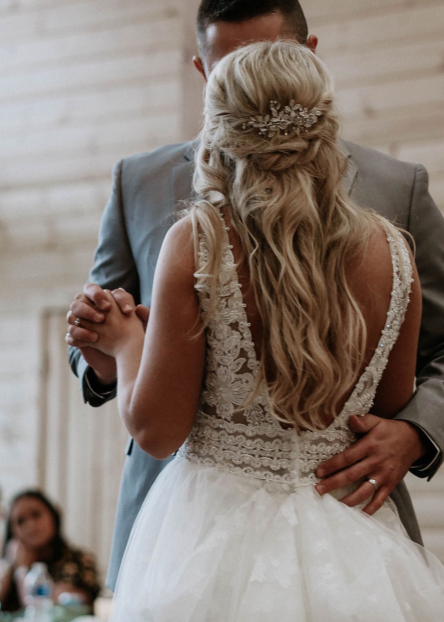Close-up of bride in backless lace gown with elegant half-up hairstyle and jeweled hair piece.