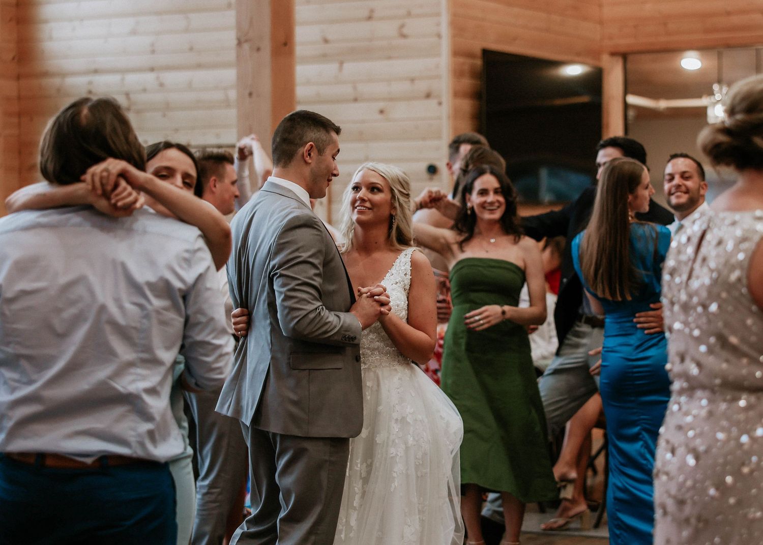Bride and groom share a dance with guests at a rustic wooden wedding reception venue.