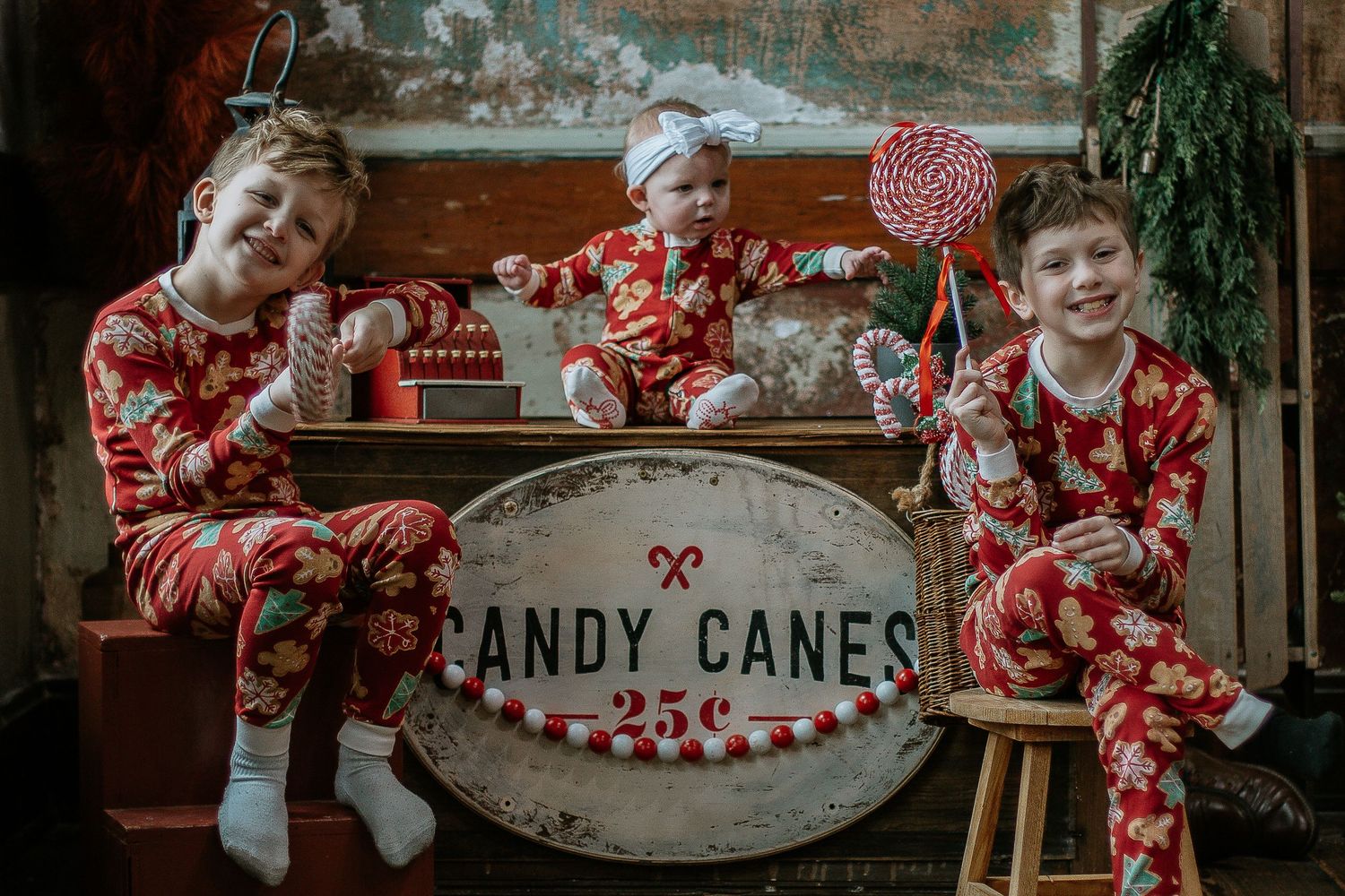 Three children in matching red Christmas pajamas pose with a vintage Candy Canes sign and holiday props at Mill Street Studios in Cincinnati