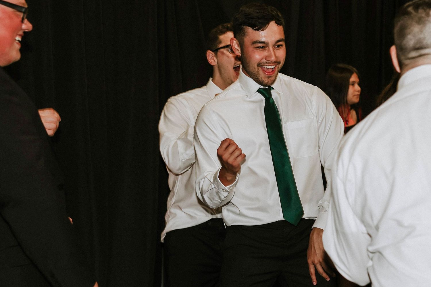 Man in white shirt and green tie dancing joyfully at a formal event or wedding reception.