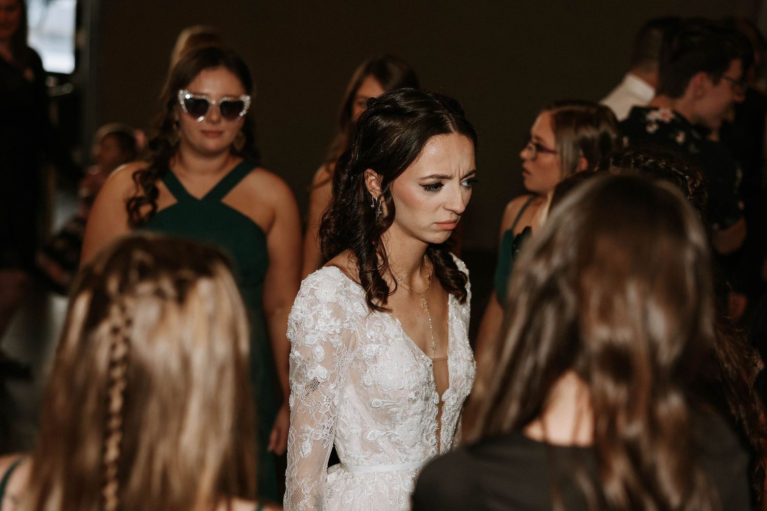 Bride in lace wedding gown surrounded by guests at elegant wedding reception.