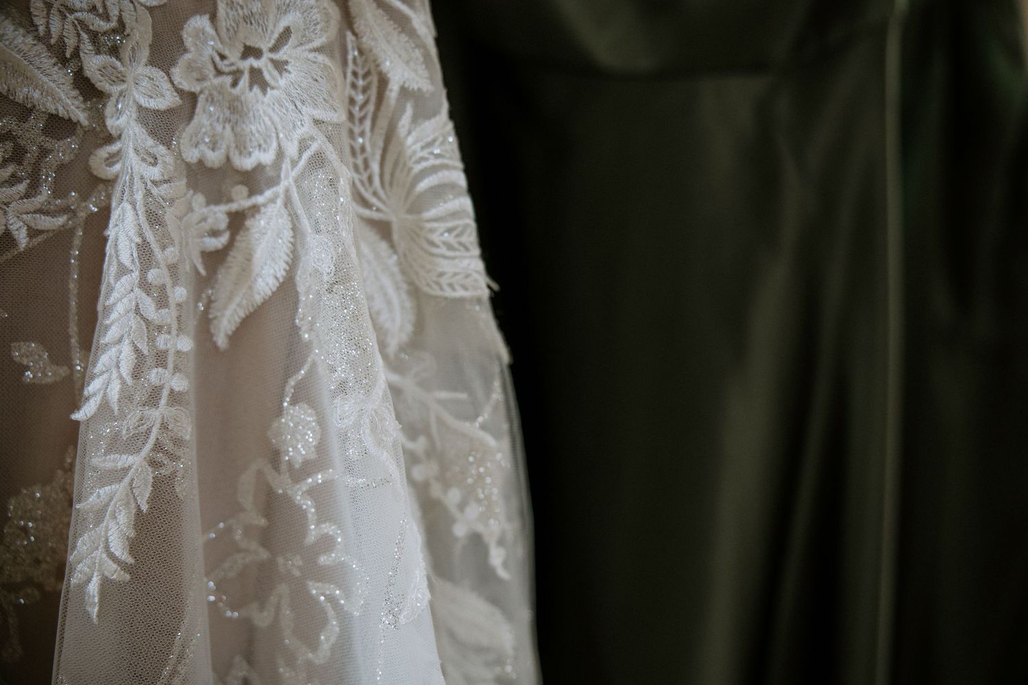 Delicate floral lace wedding gown detail contrasted against a dark green satin bridesmaid dress at Urban Artifact in Cincinnati, Ohio