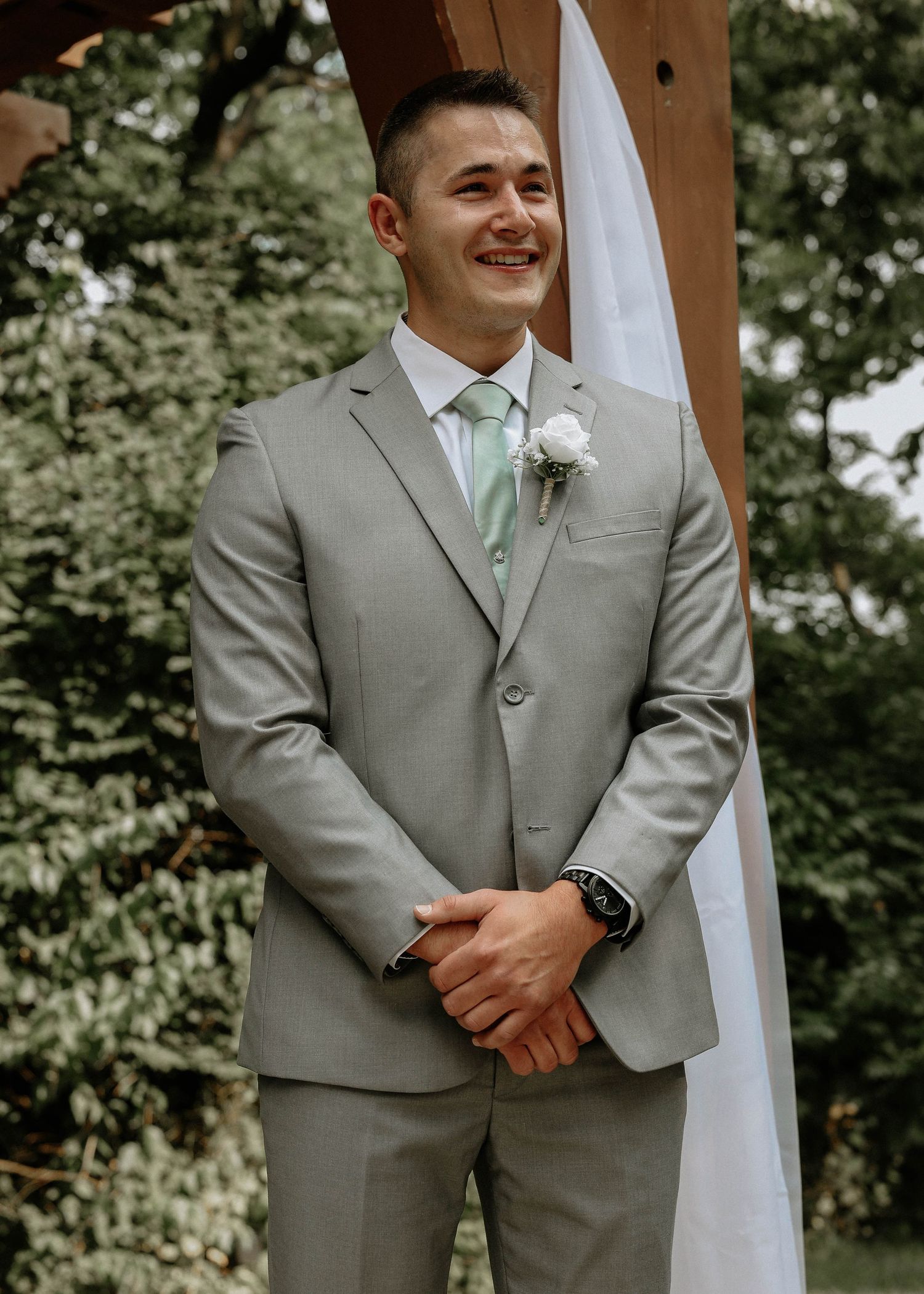 Emotional groom in gray suit with mint tie and boutonniere stands at the altar during wedding ceremony.