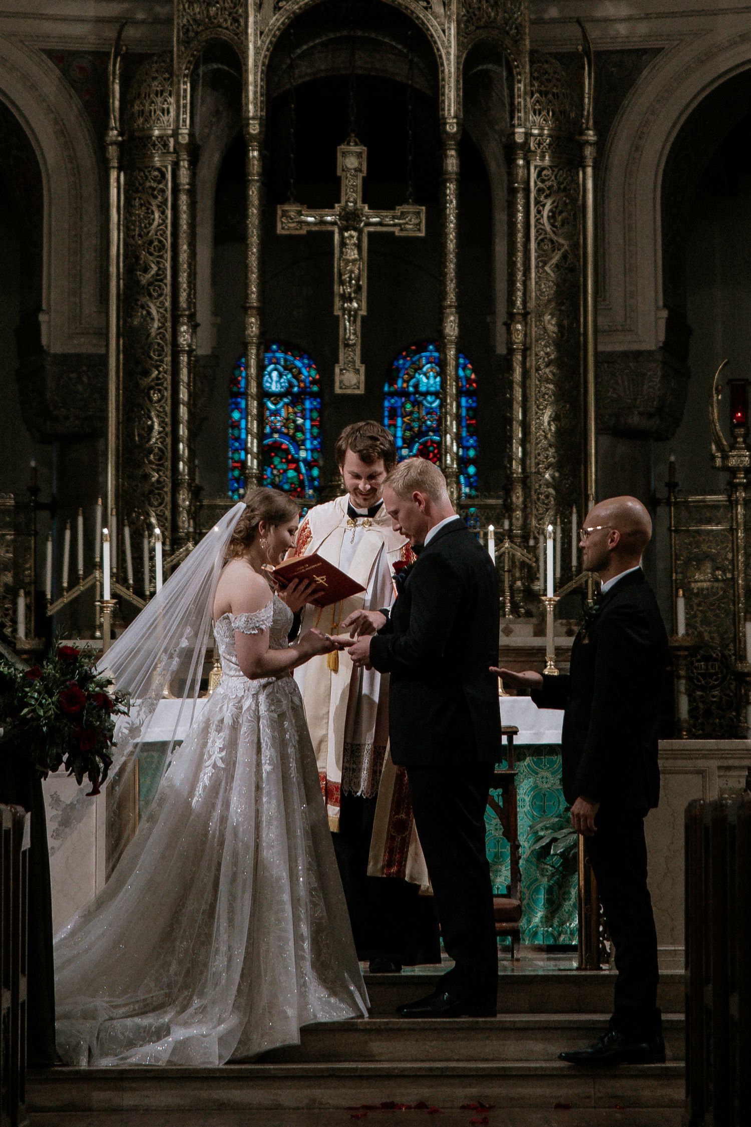 Bride and groom exchange rings before priest holding red book at ornate church altar in Cincinnati, Ohio