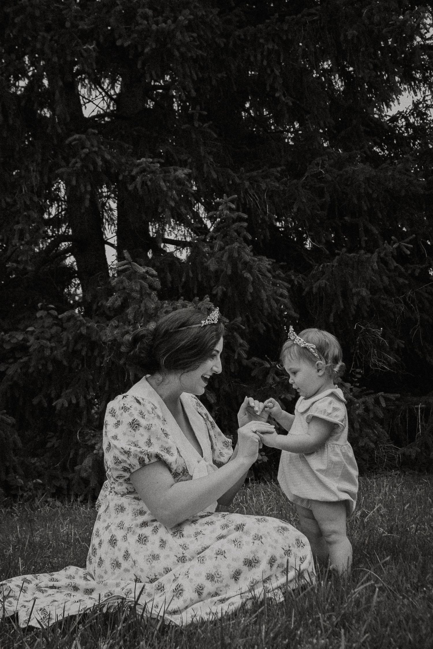 Black and white photo of mother sitting on grass interacting with smiling toddler outdoors at French Park in Cincinnati, Ohio