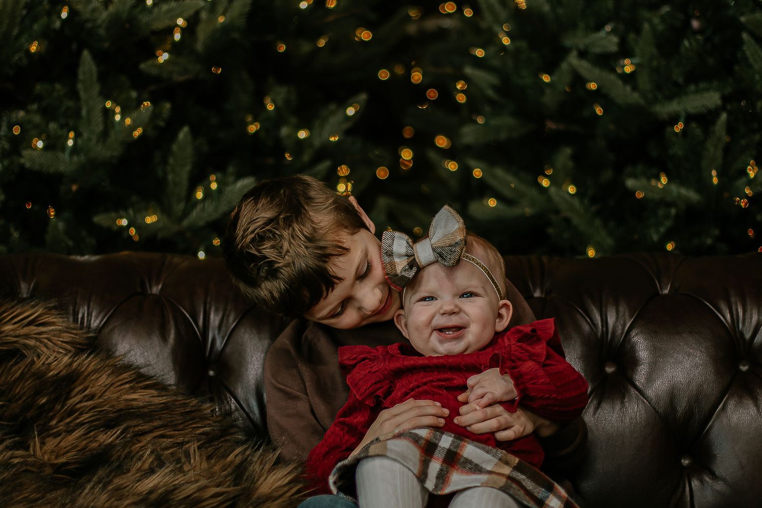 Young boy hugging and kissing a laughing baby girl on a leather sofa at Mill Street Studios in Cincinnati, Ohio.
