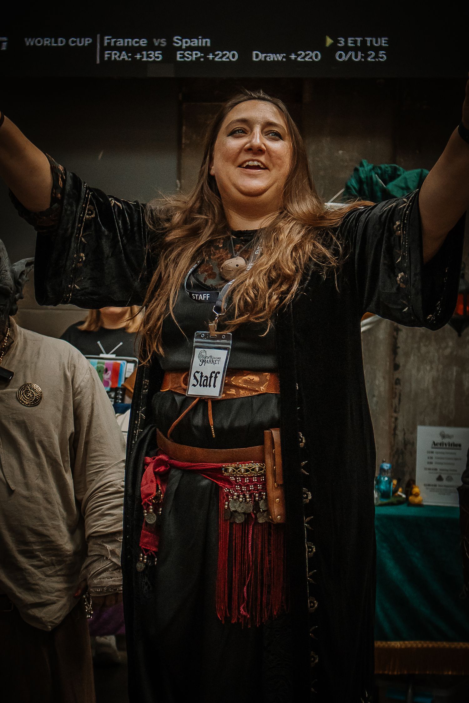 A woman in a pirate costume with a Staff badge raises her arms at a World Cup event.