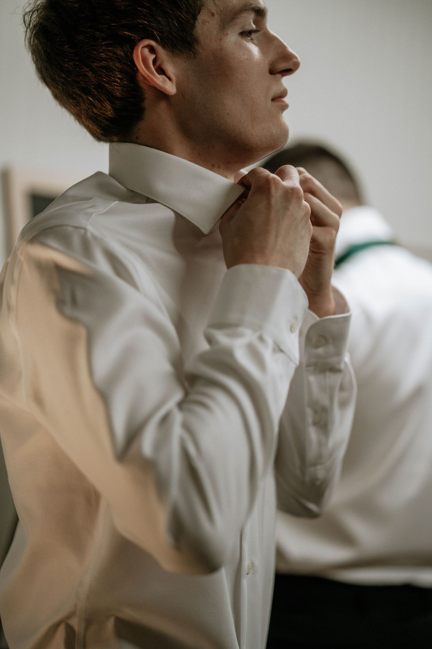 Young groom in white dress shirt adjusting his collar while getting ready for wedding ceremony.