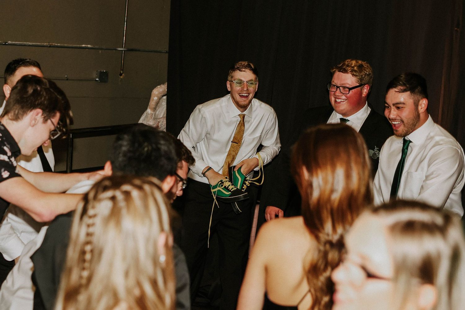 Young adults in formal attire dancing and socializing at an indoor event or prom celebration.