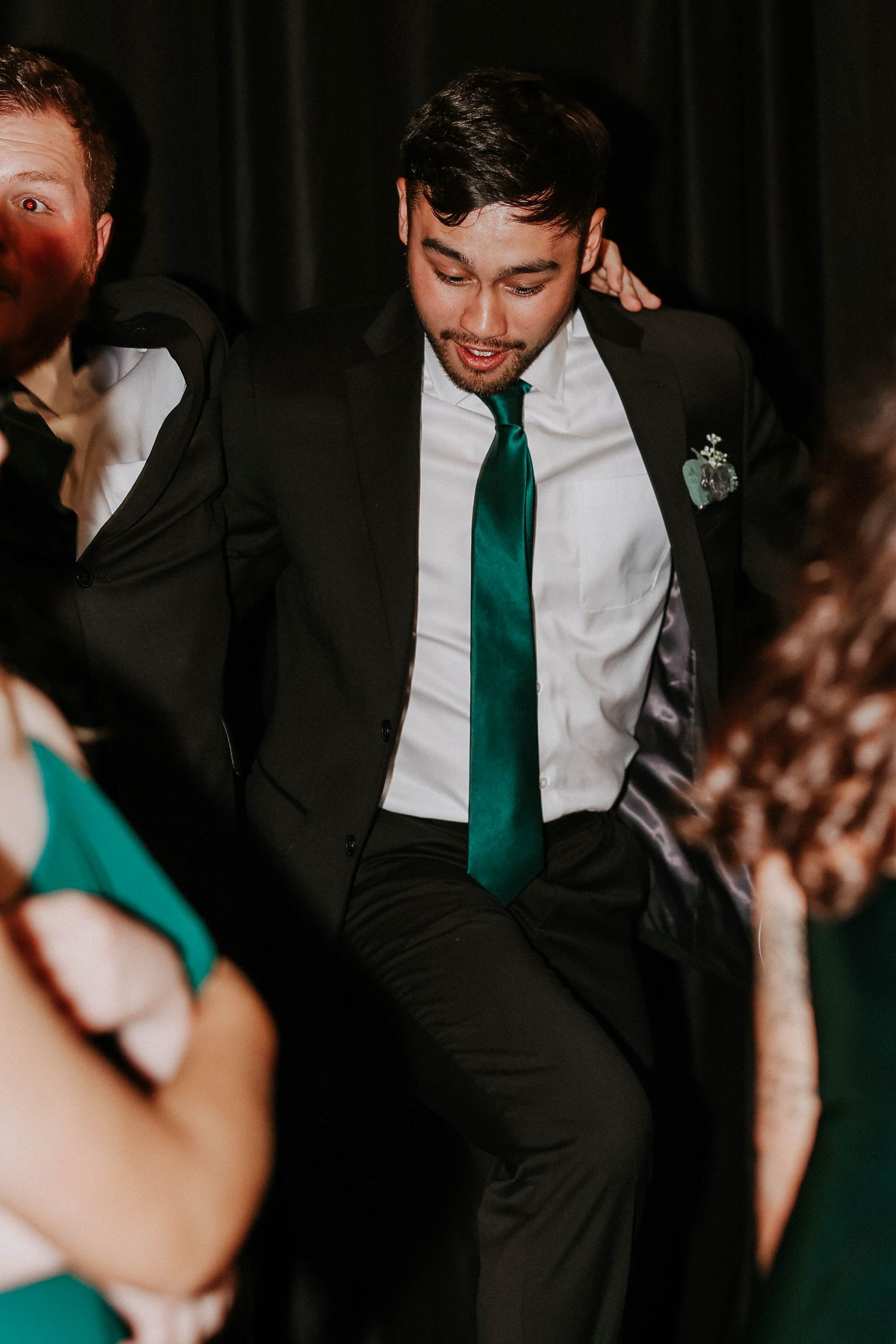 Man in black suit and green tie dancing energetically at a formal event or wedding reception.