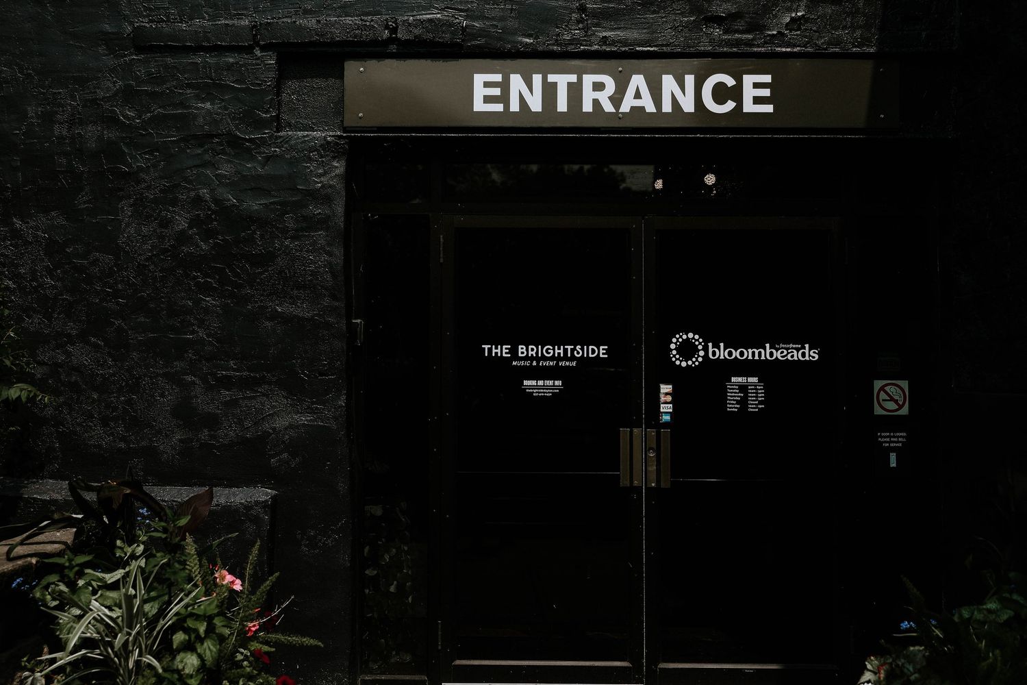 Dark entrance door of The Brightside and Bloombeads venues with illuminated ENTRANCE sign above.