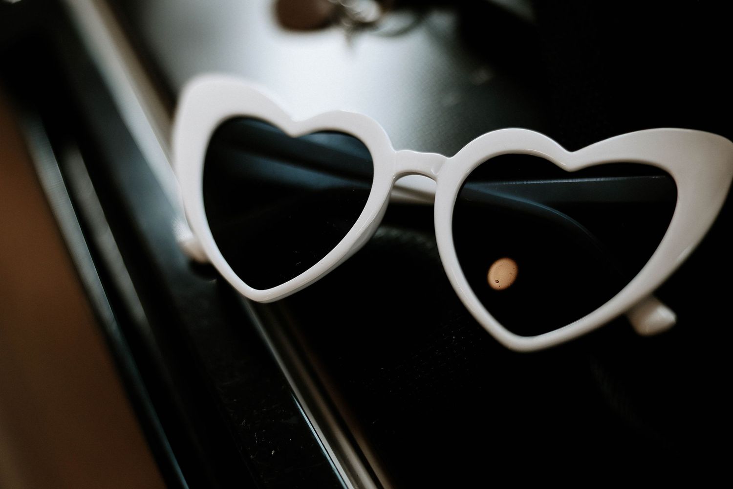 White heart-shaped sunglasses with dark lenses resting on a black surface as wedding accessories.