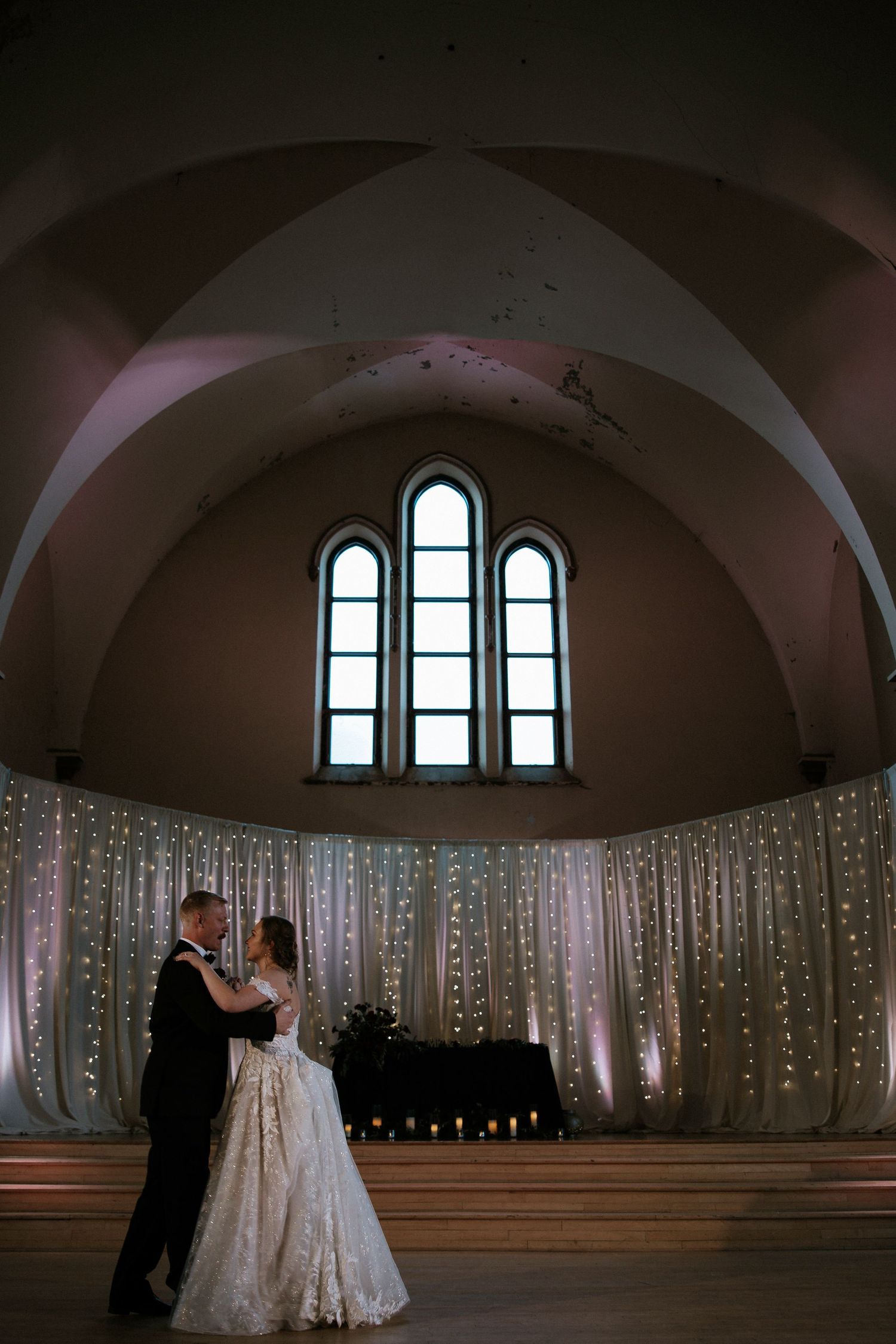Bride and groom dance romantically under arched ceiling with fairy light backdrop and candles at Urban Artifact in Cincinnati, Ohio