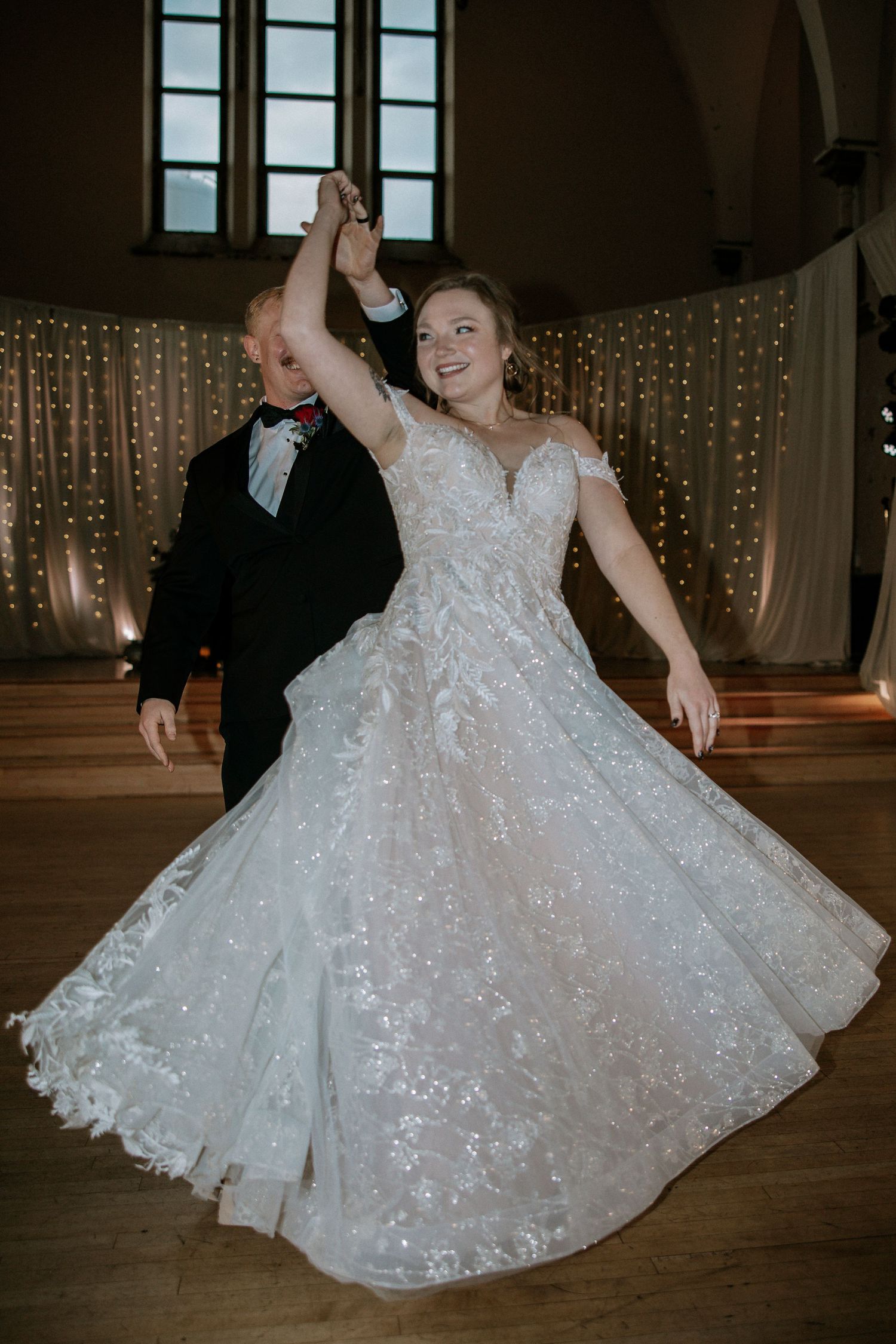 Joyful bride in sparkly lace ballgown twirls on dance floor at wedding reception at Urban Artifact in Cincinnati, Ohio