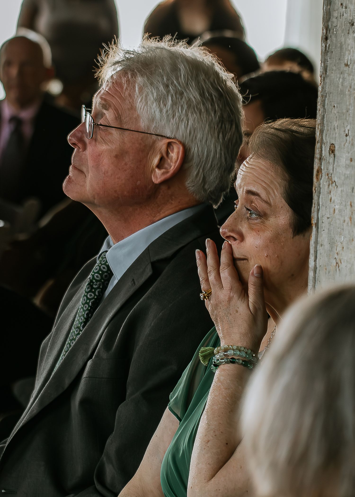 Emotional wedding guests watching ceremony, woman with hand to face and man in suit looking up at The Remedy in Dayton, Ohio