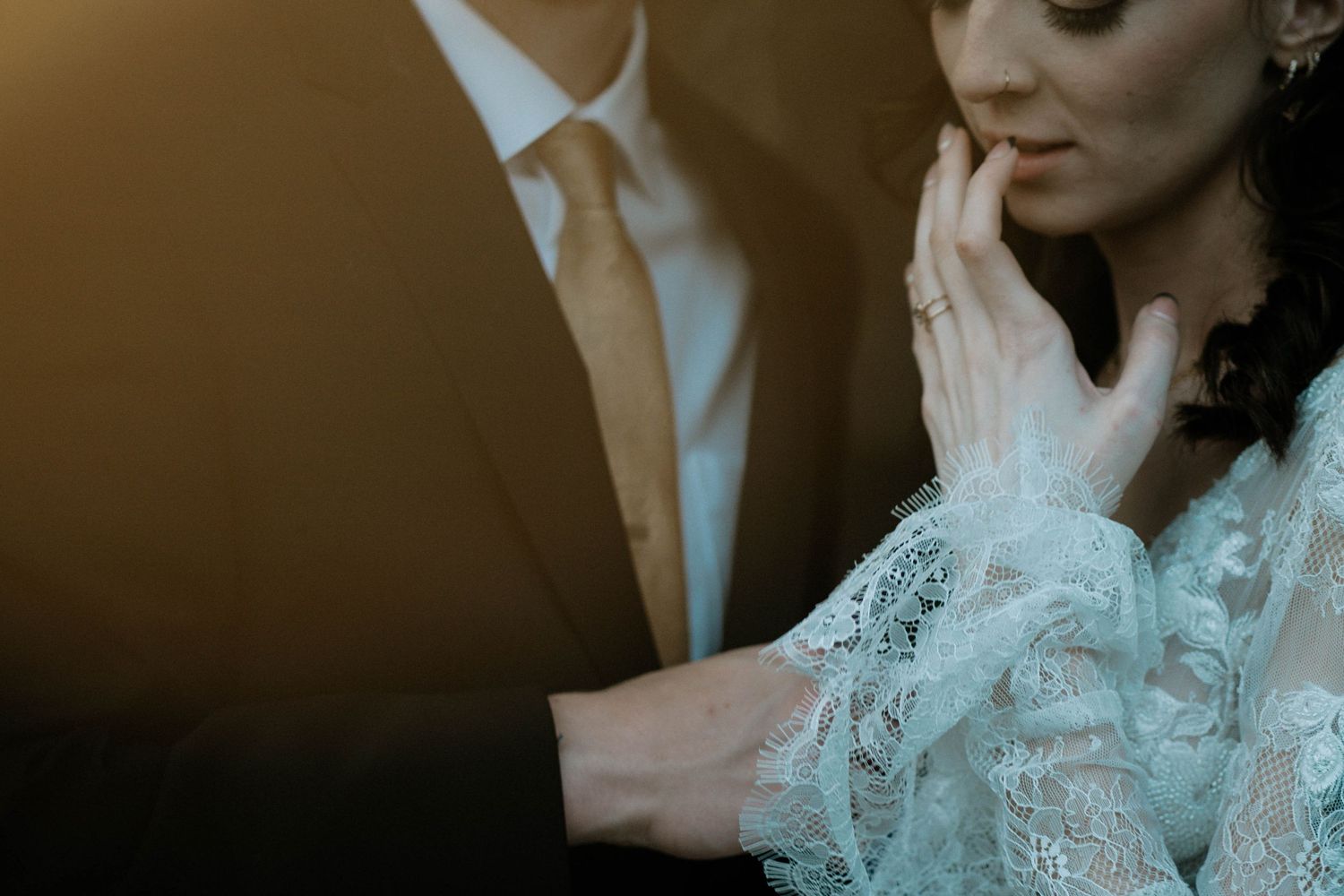 A groom tenderly touches a bride's face, her lace gown and diamond ring visible in warm light at The Brightside in Dayton, Ohio