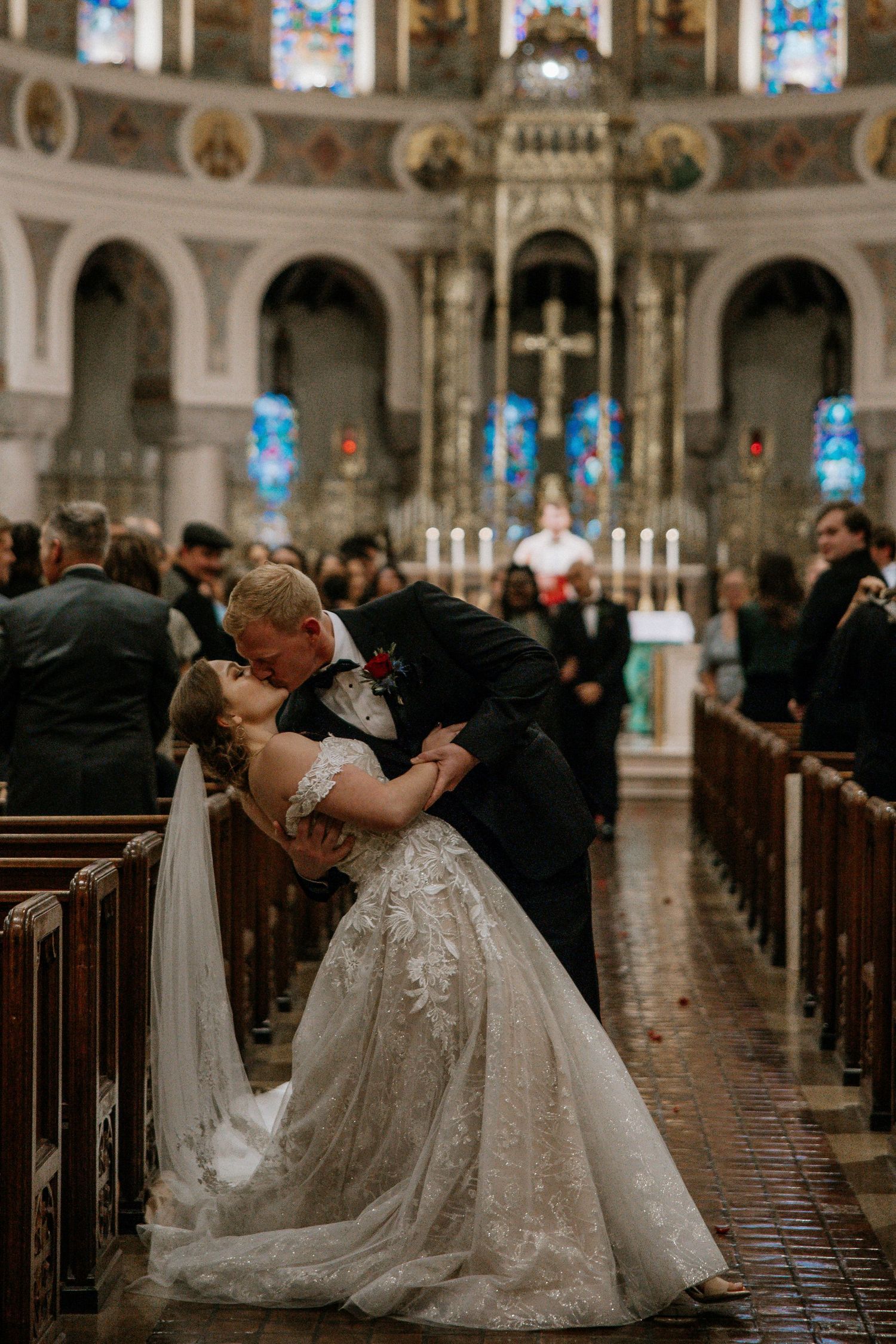 Bride and groom share a dramatic dip kiss in the aisle of an ornate church after their wedding ceremony.