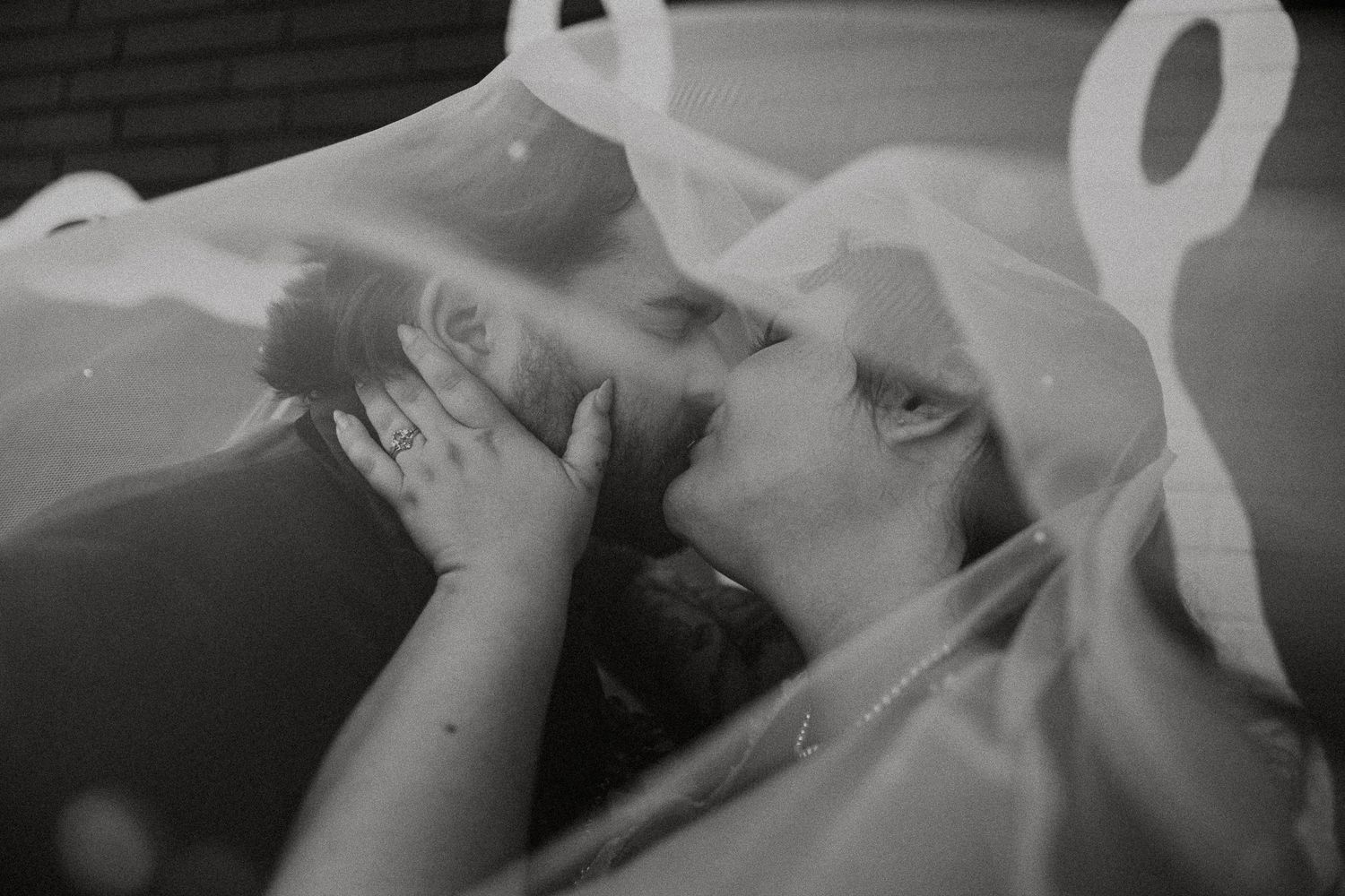 Intimate black and white close-up of bride and groom kissing beneath sheer sparkle wedding veil.