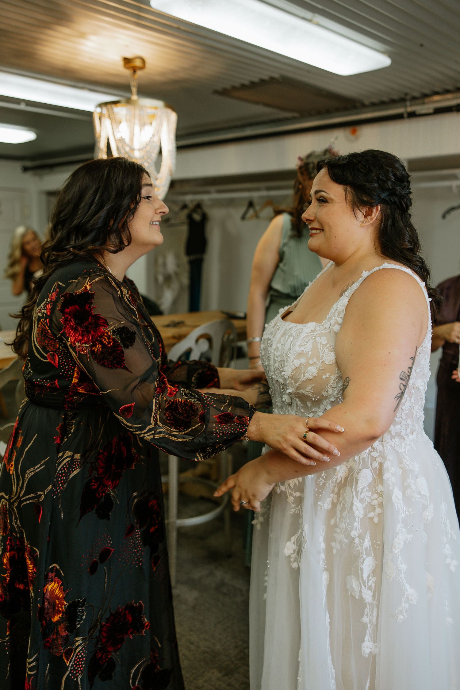 Two brides holding hands and smiling at each other during wedding preparations in a bridal suite.