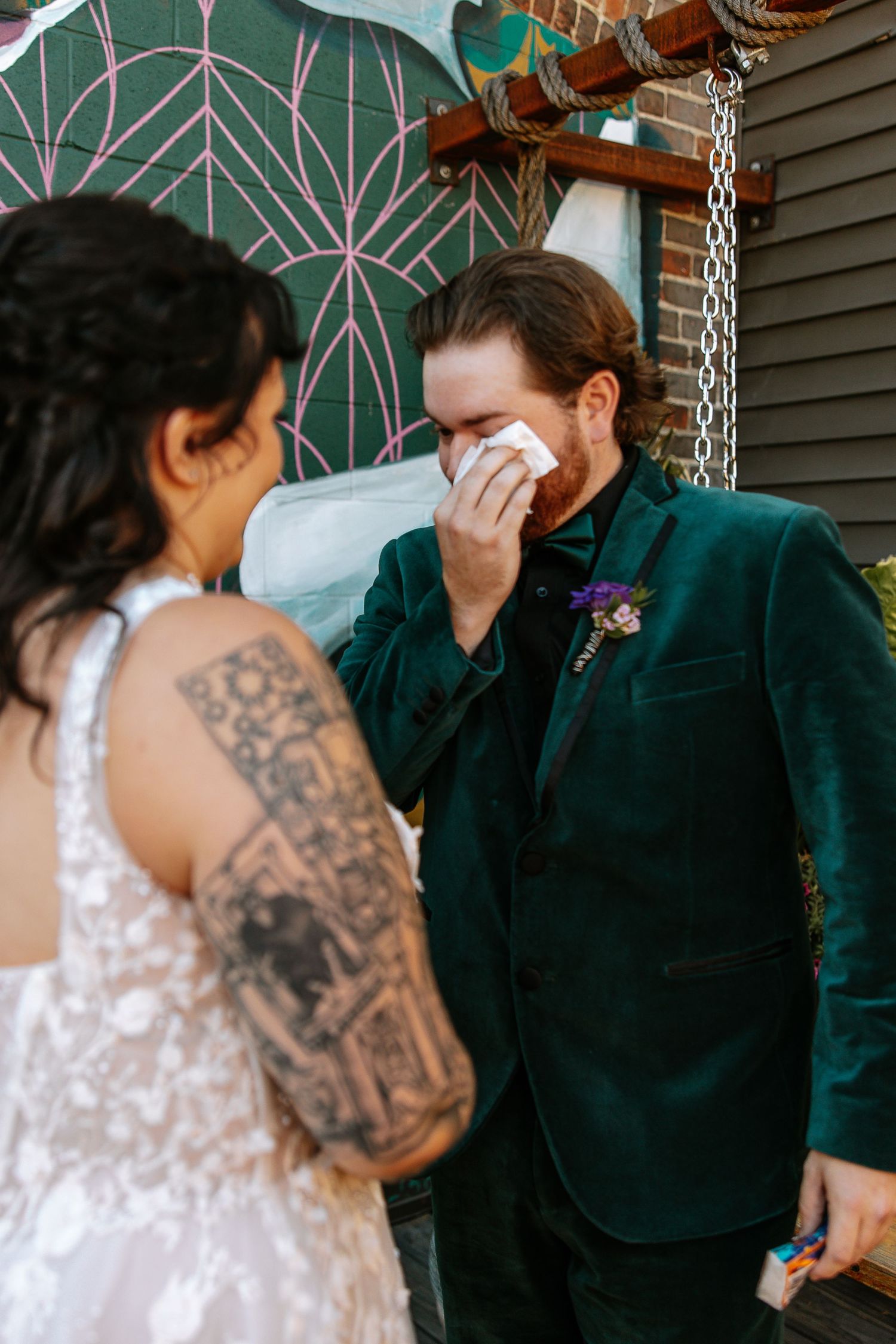 Emotional groom in green velvet suit wipes tears seeing bride in lace wedding dress during first look.