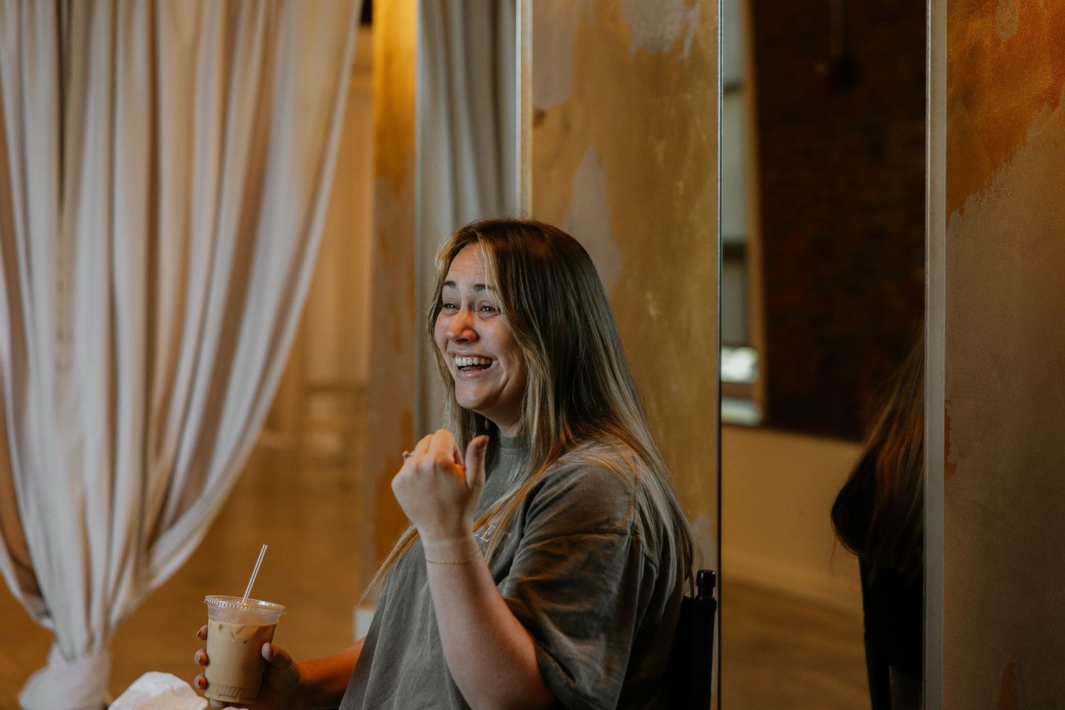Smiling woman with glasses holding an iced drink in a softly lit room.