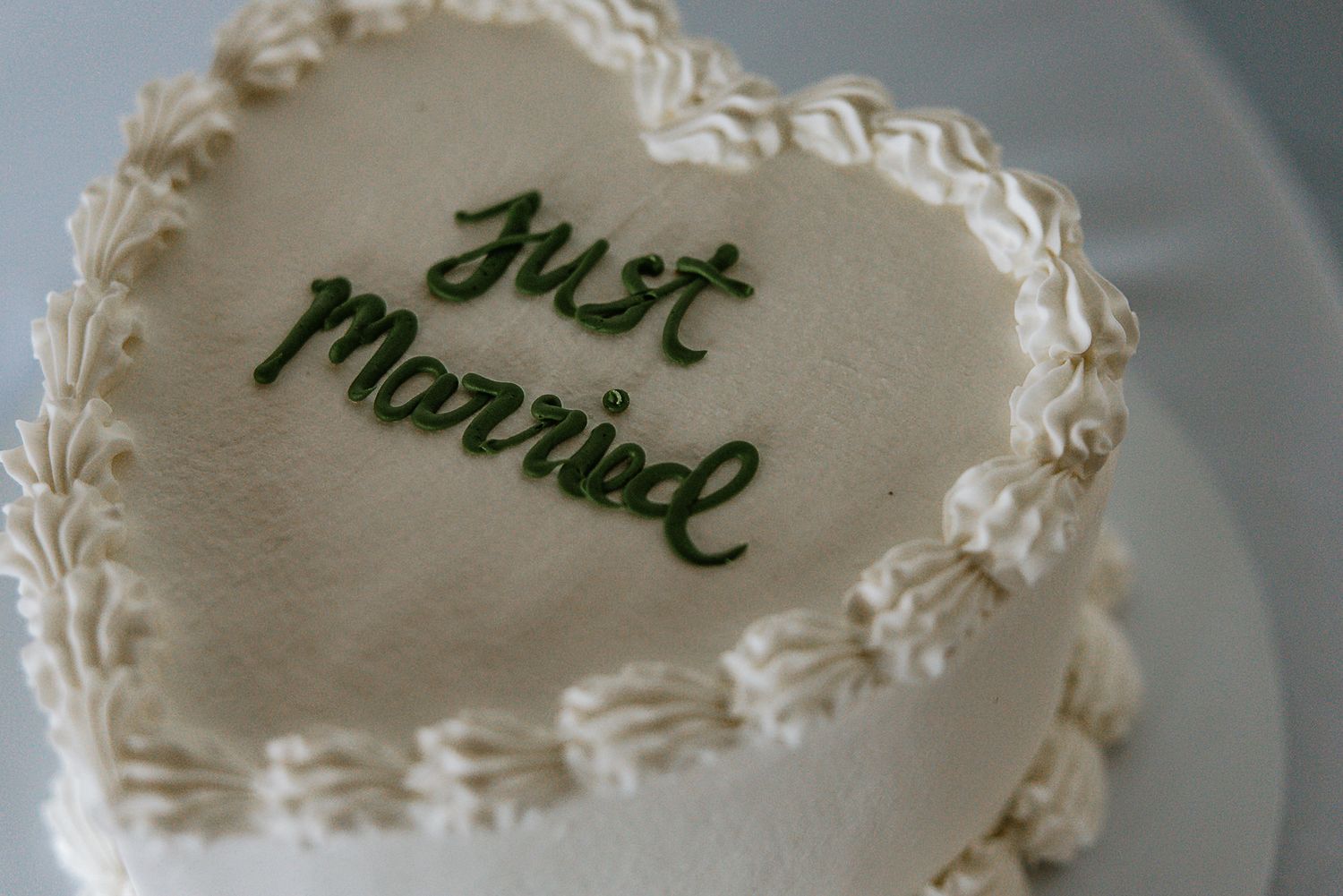 Heart-shaped white wedding cake decorated with green Just Married script frosting.