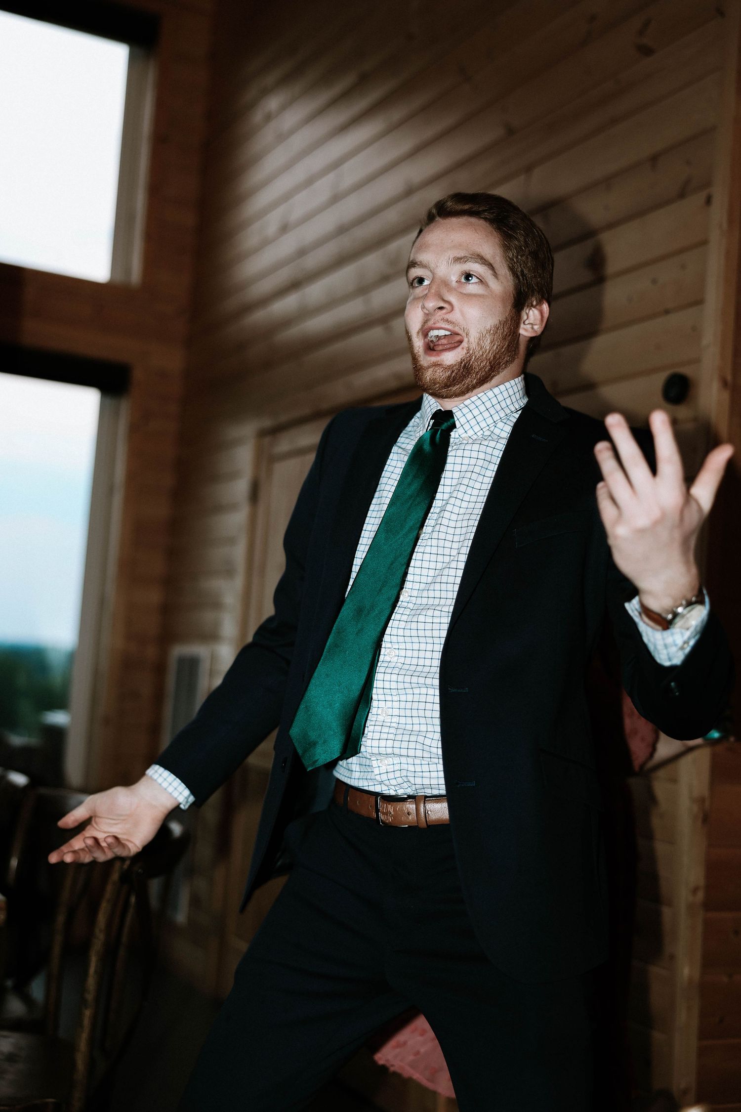 Man in black suit and green tie dancing expressively at wedding.