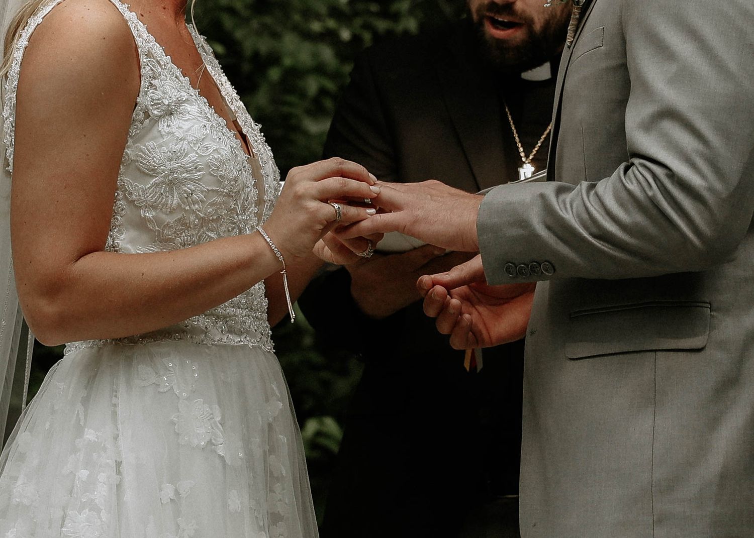 Bride and groom exchanging wedding rings during outdoor ceremony, close-up of hands.