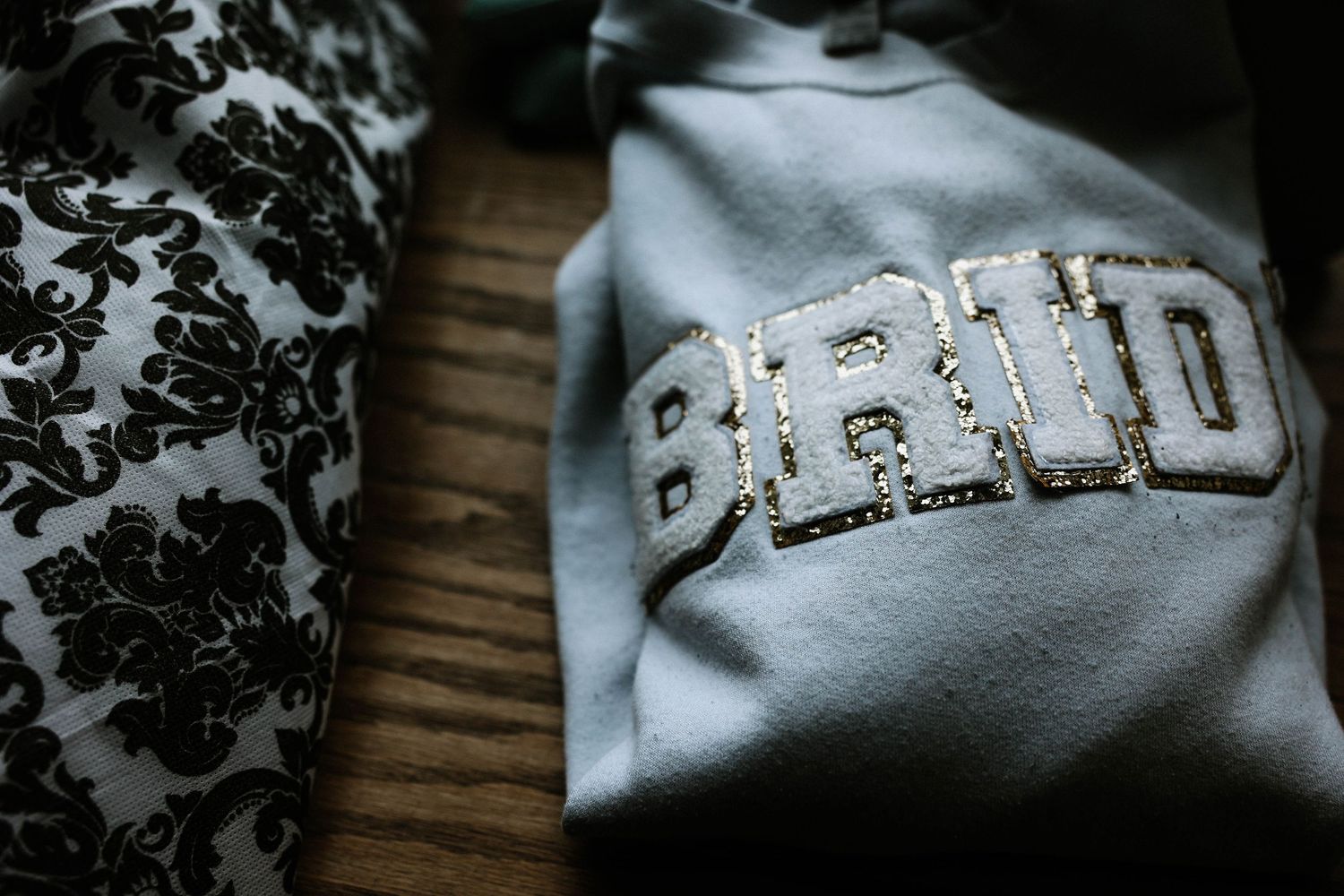 Sparkly sequin BRIDE lettering on a light blue bridal sweatshirt on wooden surface.