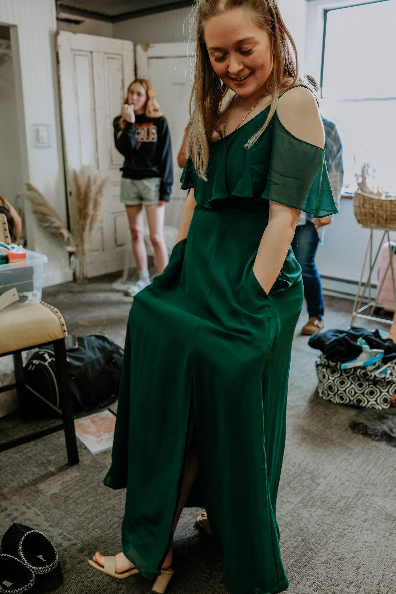 Woman smiling in elegant emerald green cold-shoulder maxi dress with pockets, standing in a dressing room.