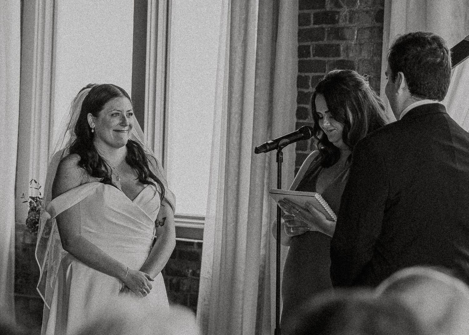 Black and white photo of bride and officiant during intimate indoor wedding ceremony.