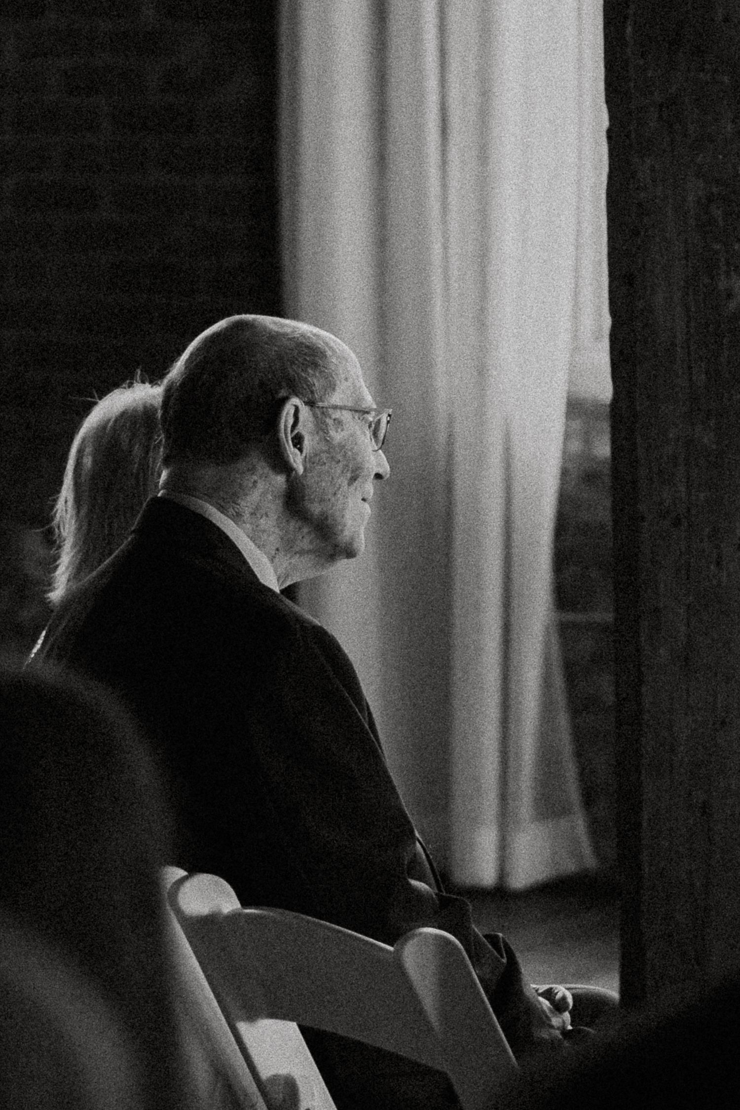 Elderly man in glasses seated at a wedding ceremony, captured in black and white.