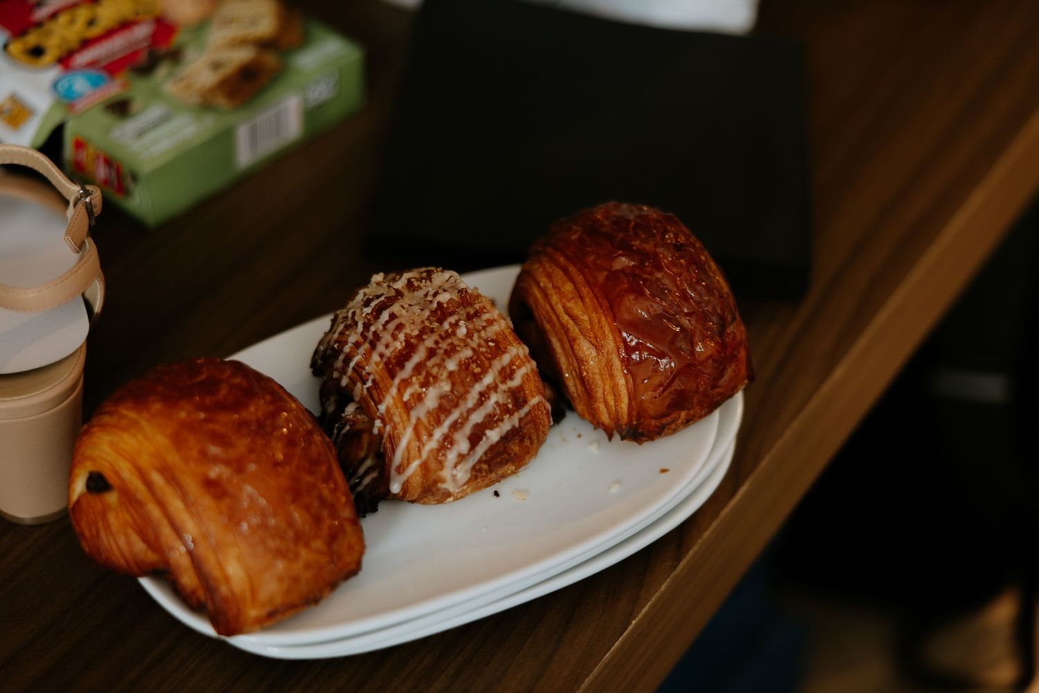 Three assorted pastries including croissants on a white plate on a wooden table.