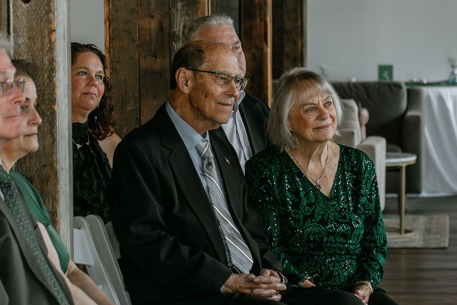 Elderly couple smiling warmly while seated together at a wedding ceremony.