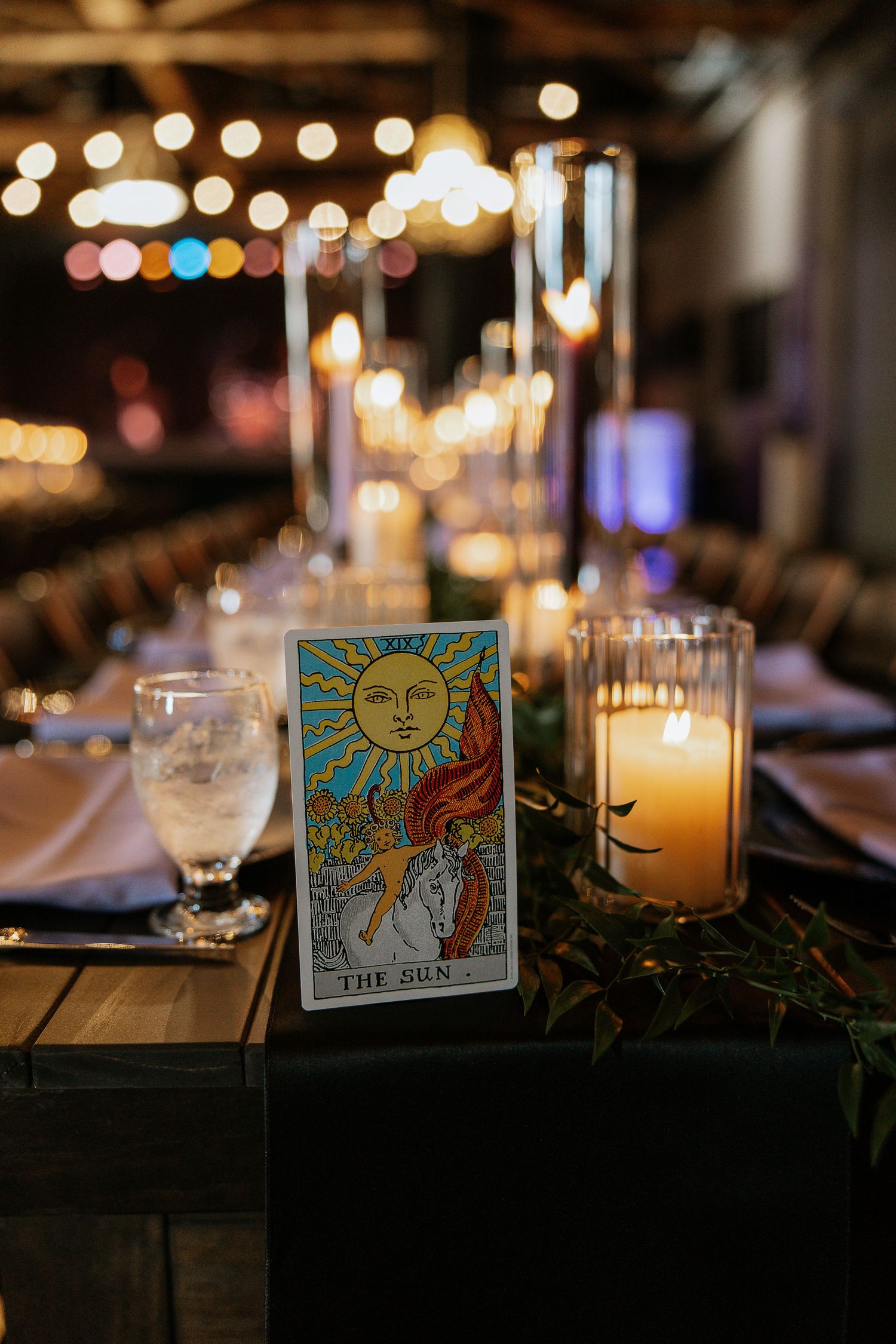Tarot card table number display with The Sun card beside glowing candles at a moody wedding reception.