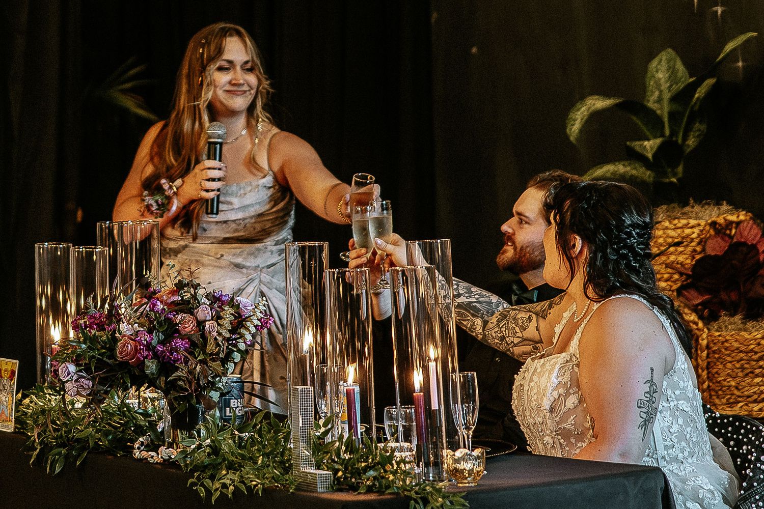 Two brides share a joyful moment at their candlelit wedding reception sweetheart table.