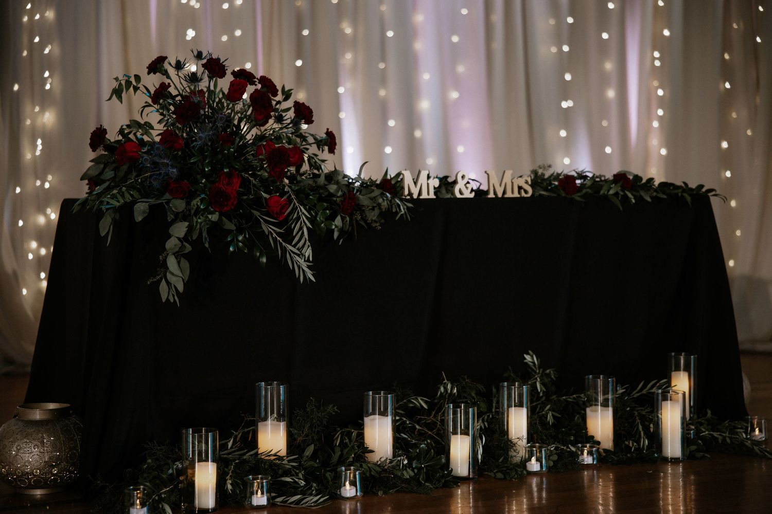 Elegant wedding sweetheart table with black linen, red floral arrangements, candles, and Mr & Mrs sign at Urban Artifact in Cincinnati, Ohio