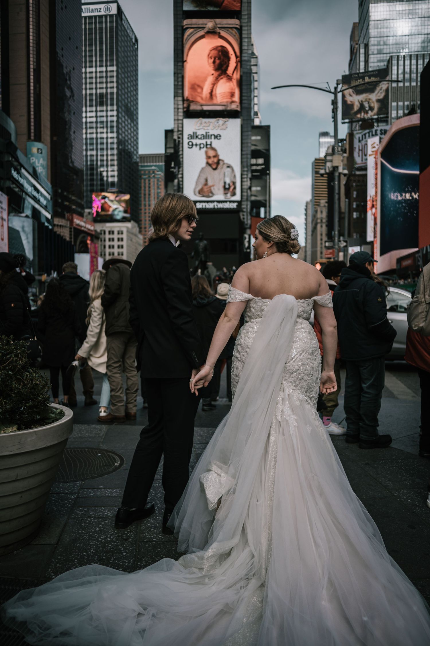 Bride in lace mermaid wedding gown with long train walking with groom through Times Square NYC.