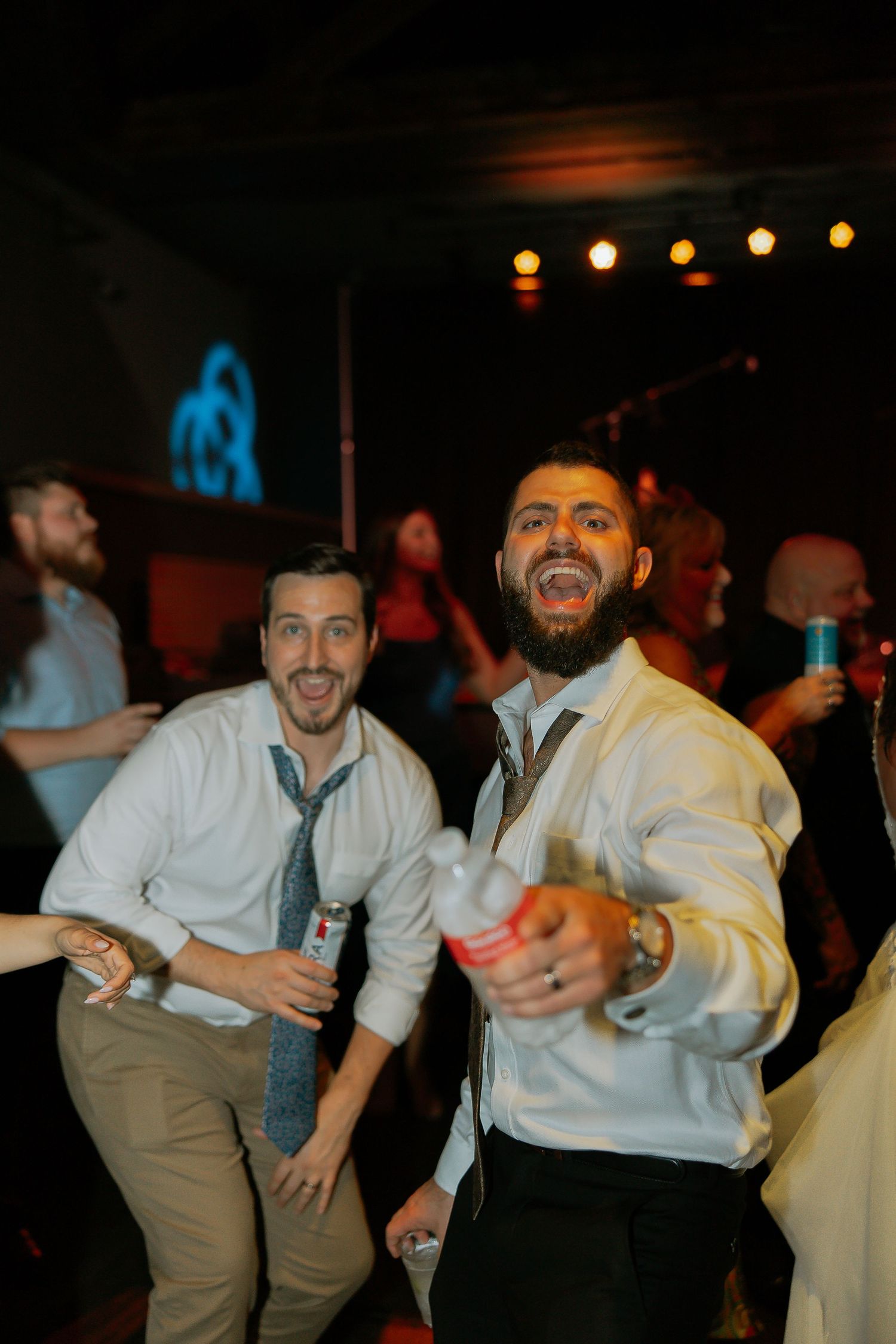 Two men in dress shirts smiling and dancing energetically at a wedding reception party.