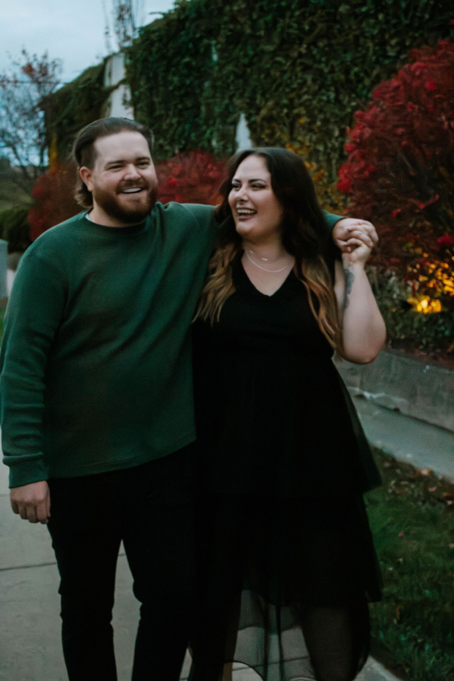 A couple walks together outdoors,  with vibrant red autumn foliage in the background in West Third Street Historic District in Dayton, Ohio