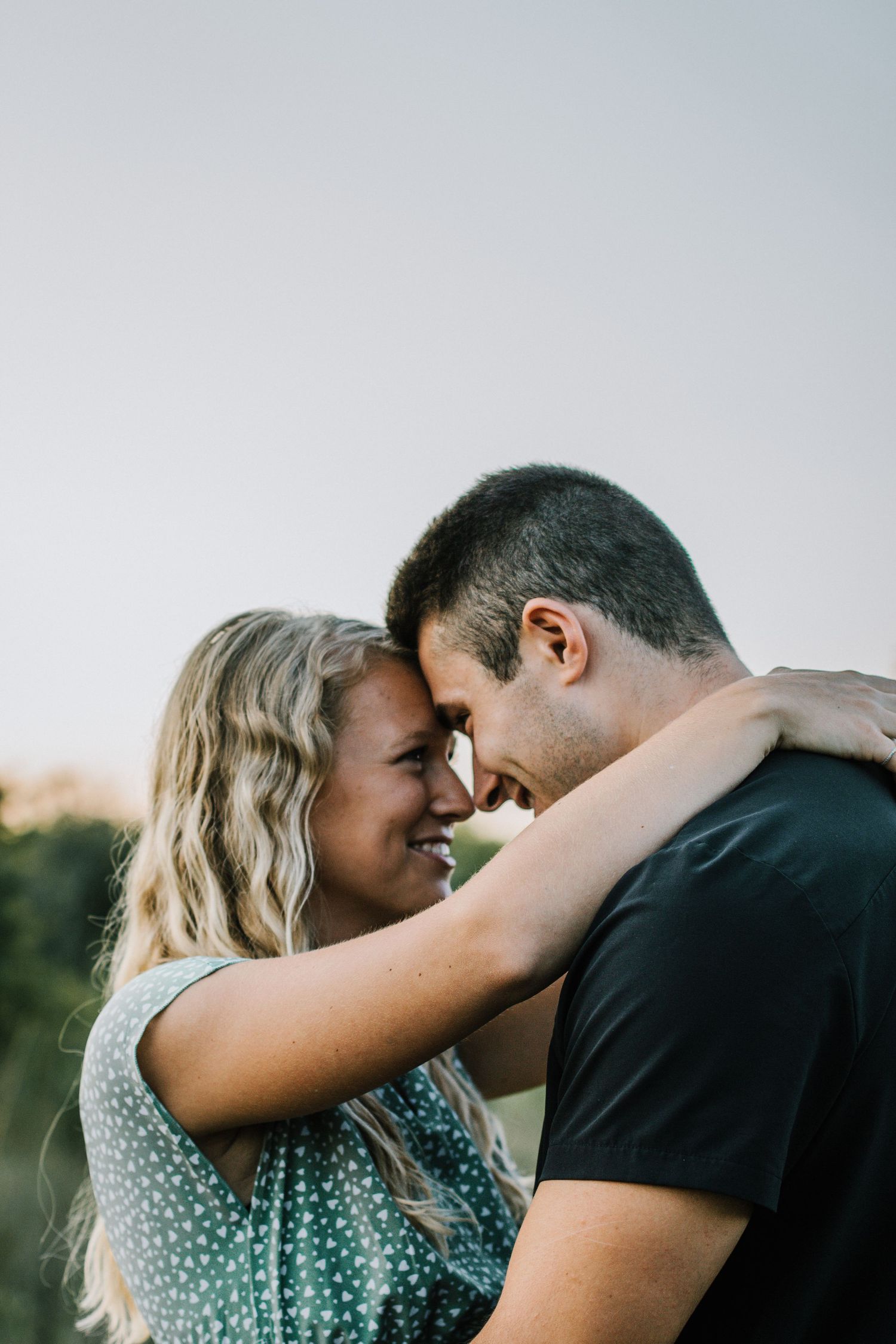 A smiling couple shares a tender forehead-to-forehead moment outdoors at golden hour at Oakes Quarry Park in Dayton, Ohio