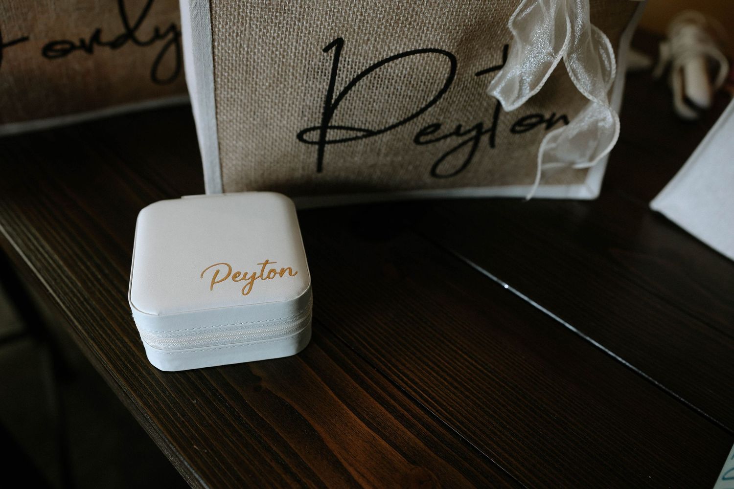White personalized jewelry box with Peyton name in gold script beside a matching monogrammed burlap tote bag.