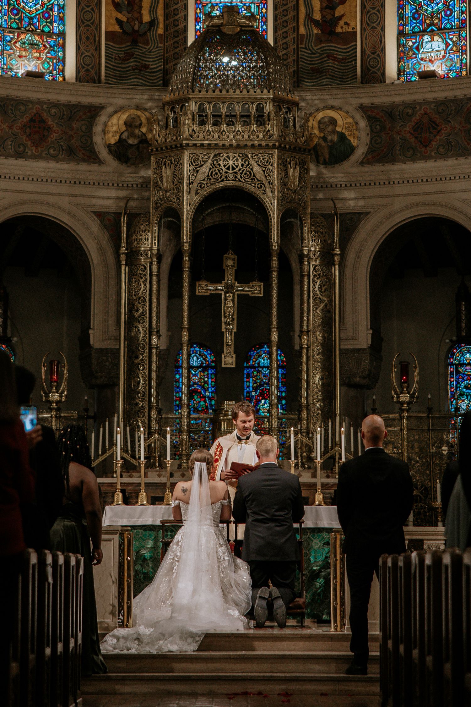 Bride and groom kneeling at elaborately decorated Catholic church altar during wedding ceremony in Cincinnati, Ohio