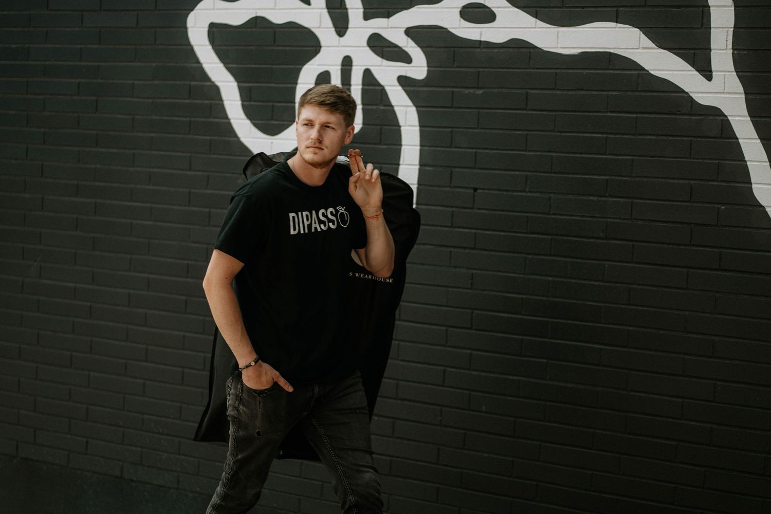 Young man in black Dipass t-shirt posing confidently against dark brick wall with white graffiti art at The Brightside in Dayton, Ohio