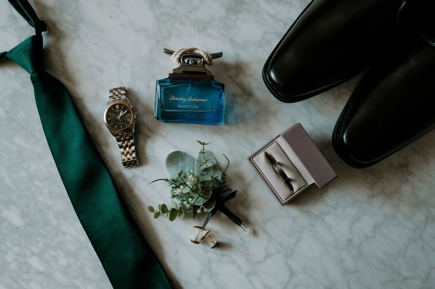 Elegant groom wedding flat lay featuring green tie, watch, cologne, boutonniere, rings, and black shoes at The Red Space in Cleveland, Ohio