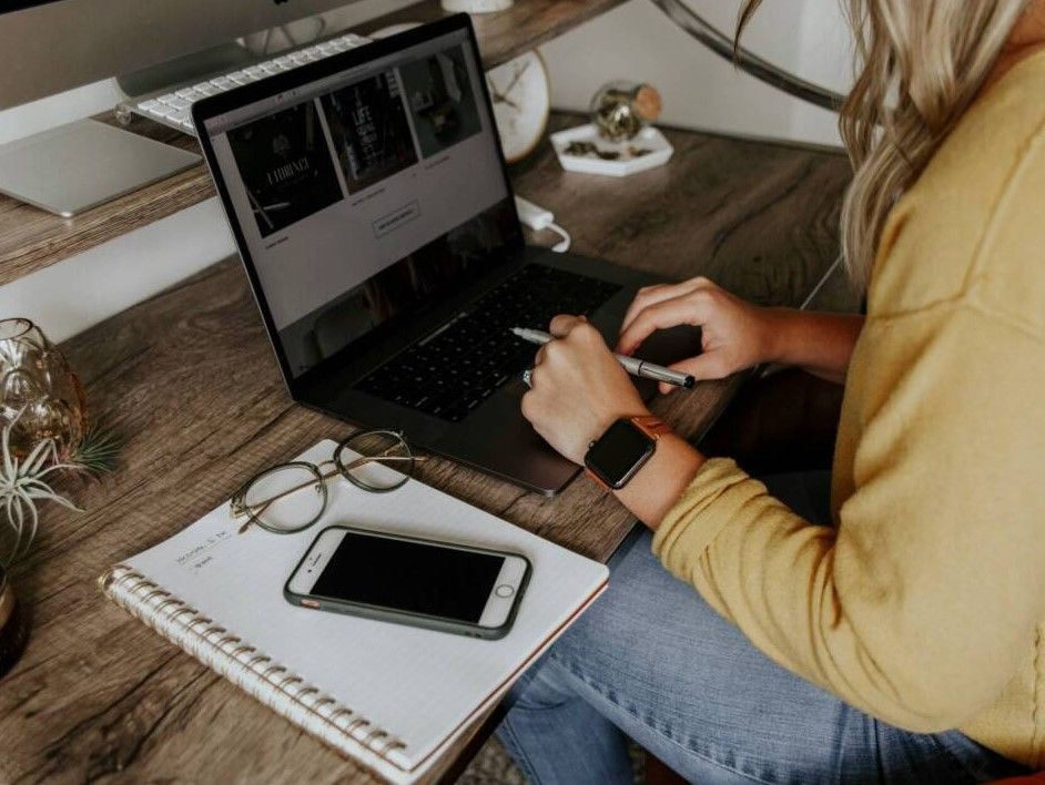 Woman in yellow sweater working on a laptop at a wooden desk with phone and notebook nearby in Cincinnati, Ohio.