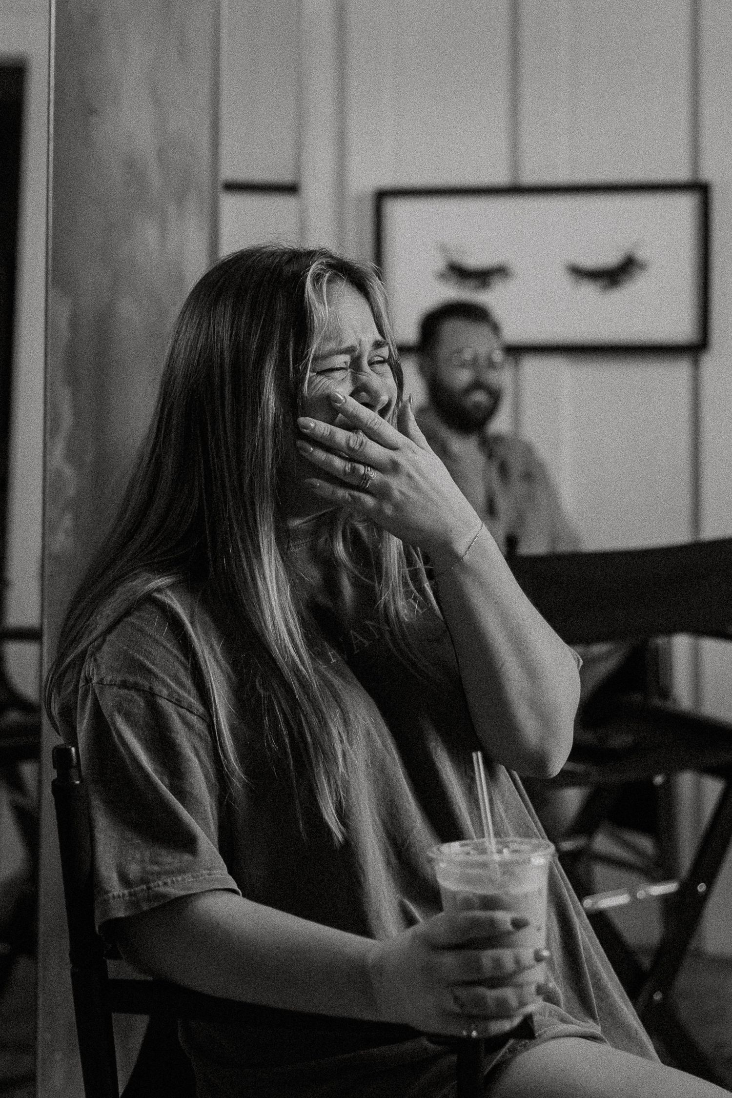 Black and white photo of a laughing woman holding an iced beverage in a chair.