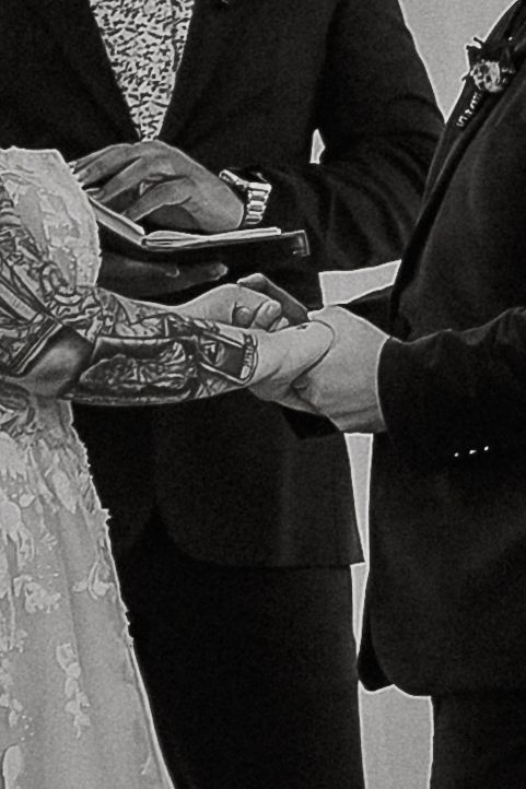 Close-up black and white photo of tattooed bride and groom exchanging wedding rings.