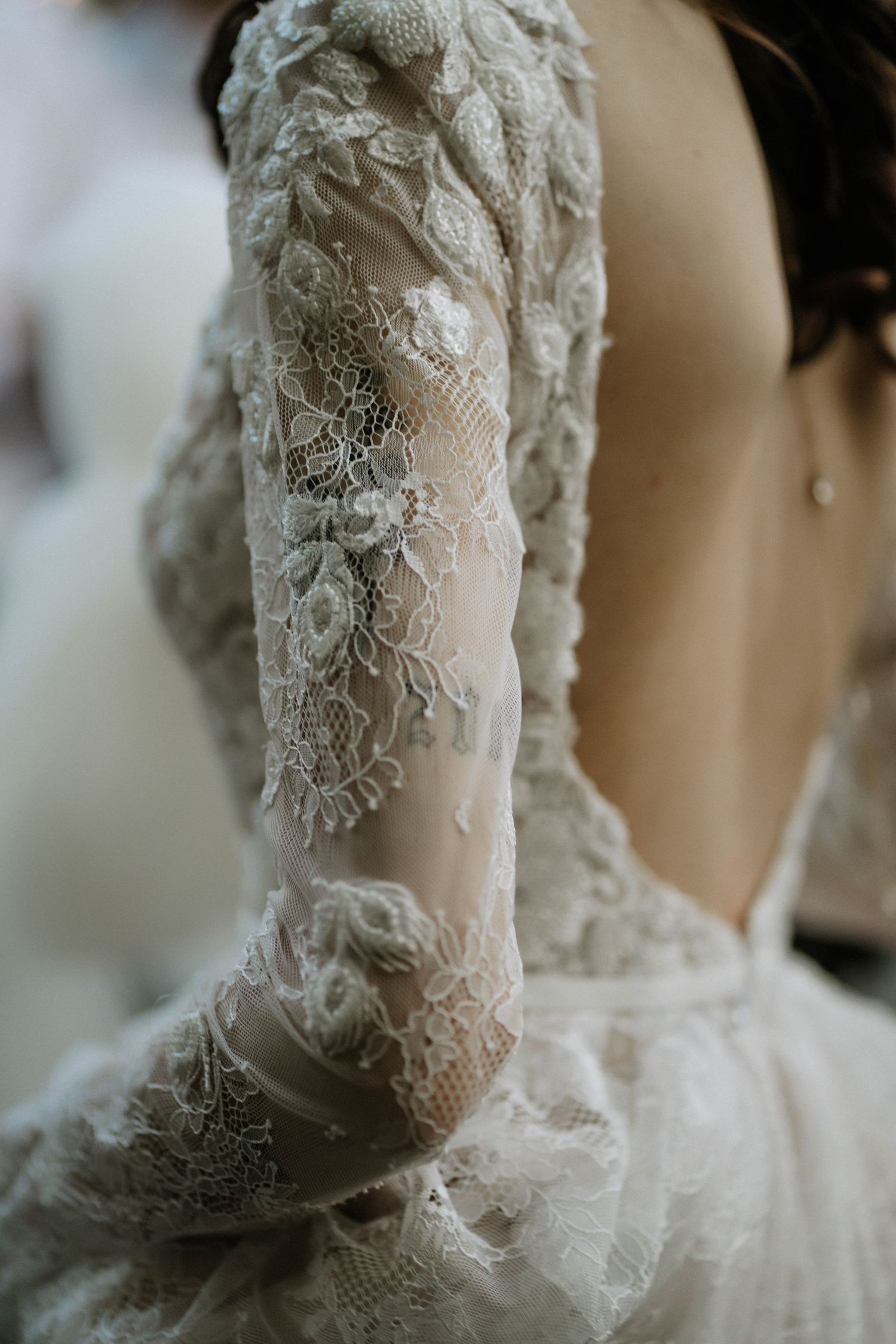 Close-up of an elegant bridal gown featuring intricate floral lace long sleeves and an open back design.
