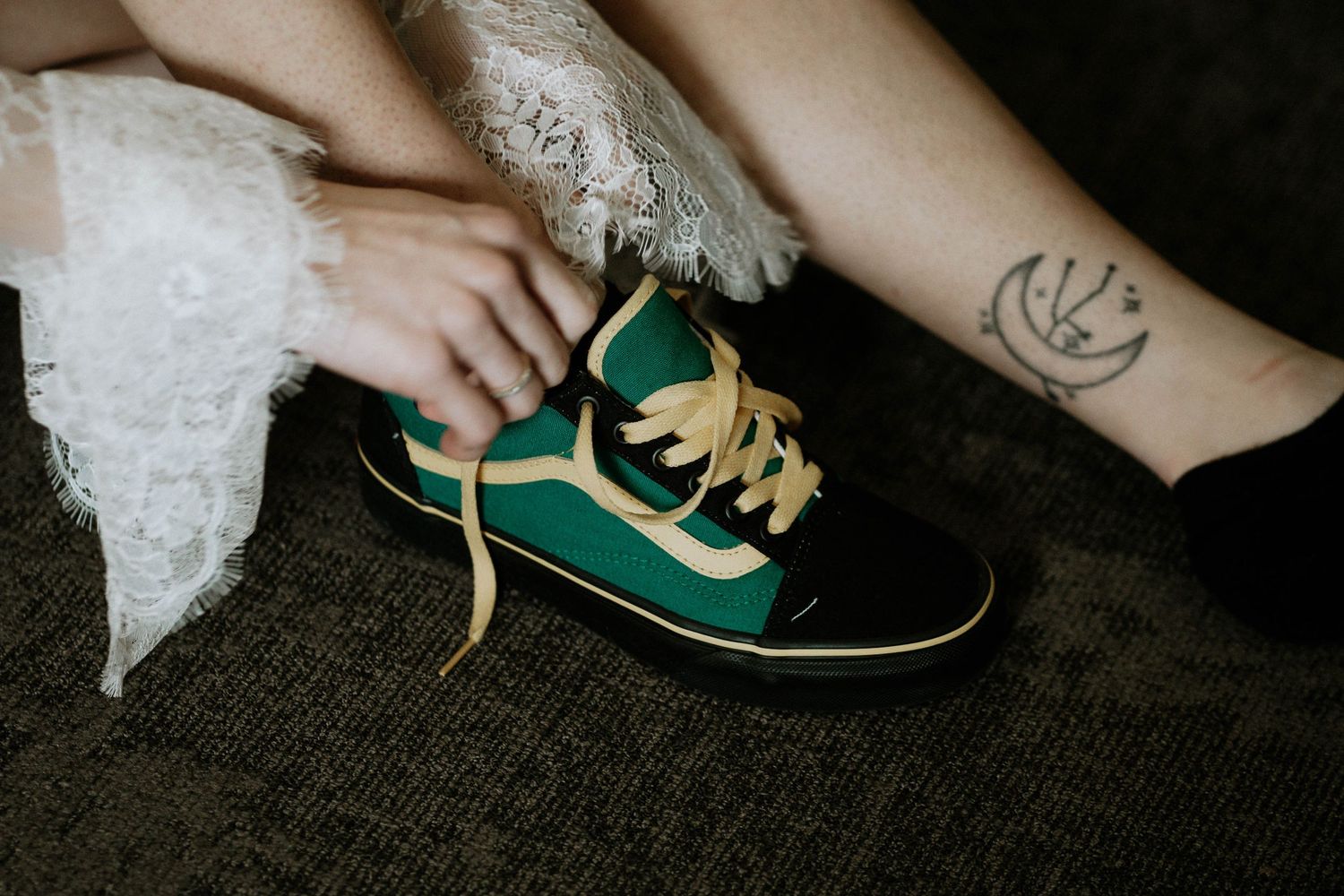 Person wearing a green and black Vans sneaker with gold laces, with a small tattoo visible on their ankle.